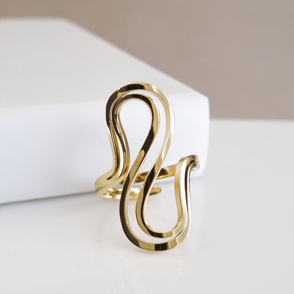 A high-polish 18K gold-plated, size-adjustable sculptural wave ring displayed on a minimalist white surface.