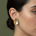A woman with a sleek bun wearing large, 18K gold-plated, hammered texture oval statement stud earrings.