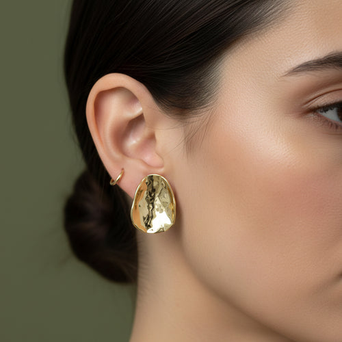 A woman with a sleek bun wearing large, 18K gold-plated, hammered texture oval statement stud earrings.