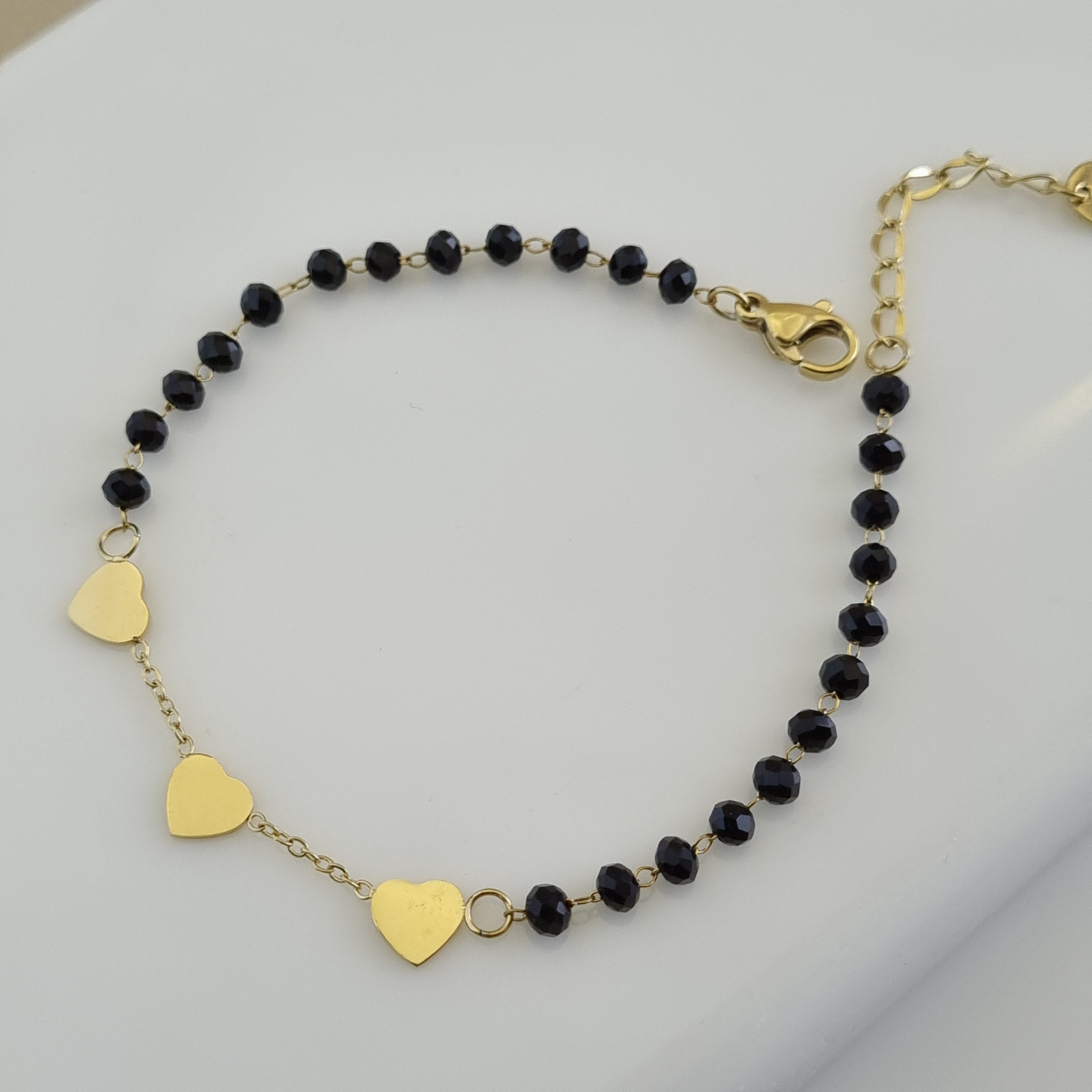 Treshire 18K gold plated Amara Hearts hand mangalsutra with faceted black beads and three gold heart charms on a white surface.