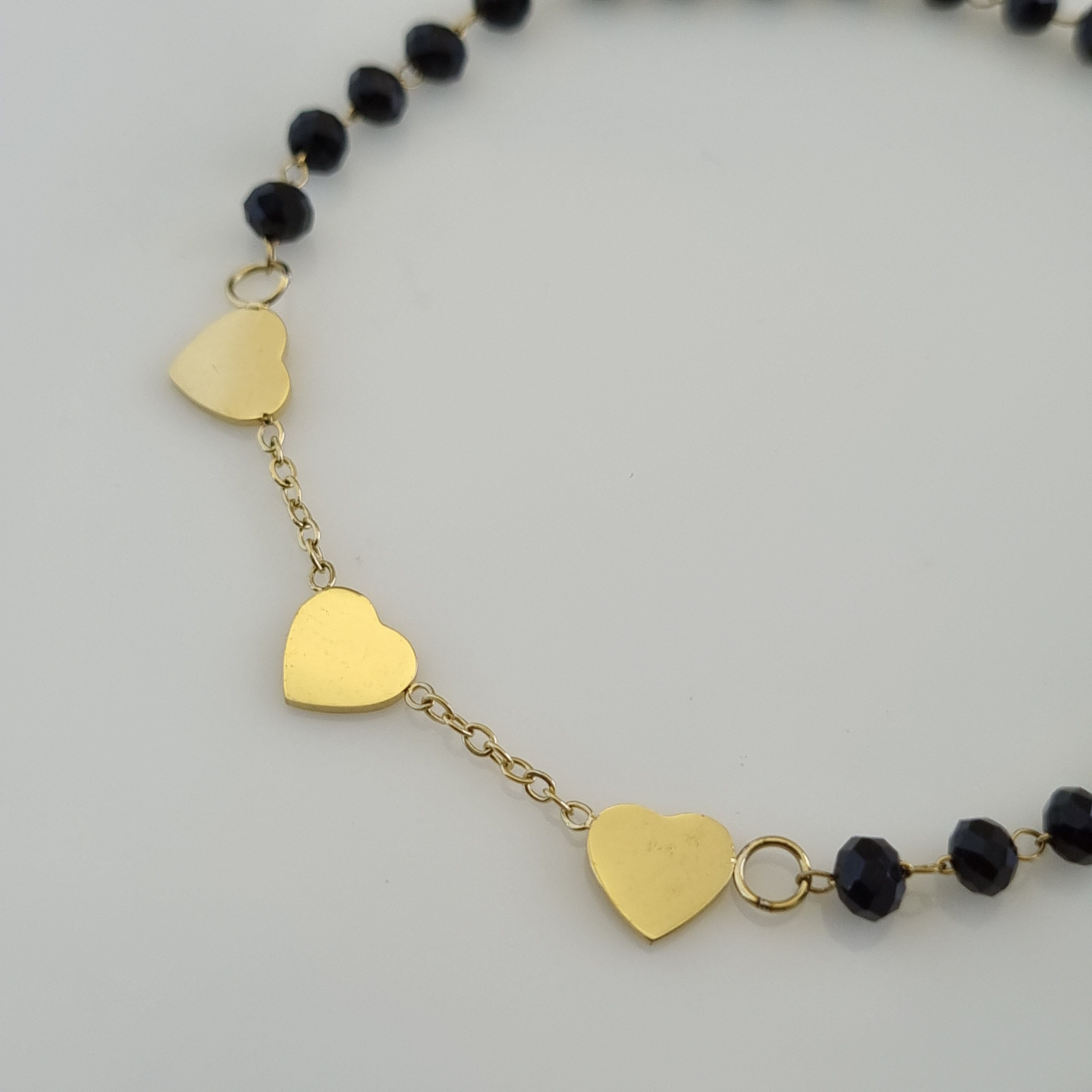 Treshire 18K gold plated Amara Hearts hand mangalsutra with faceted black beads and three gold heart charms on a white surface.