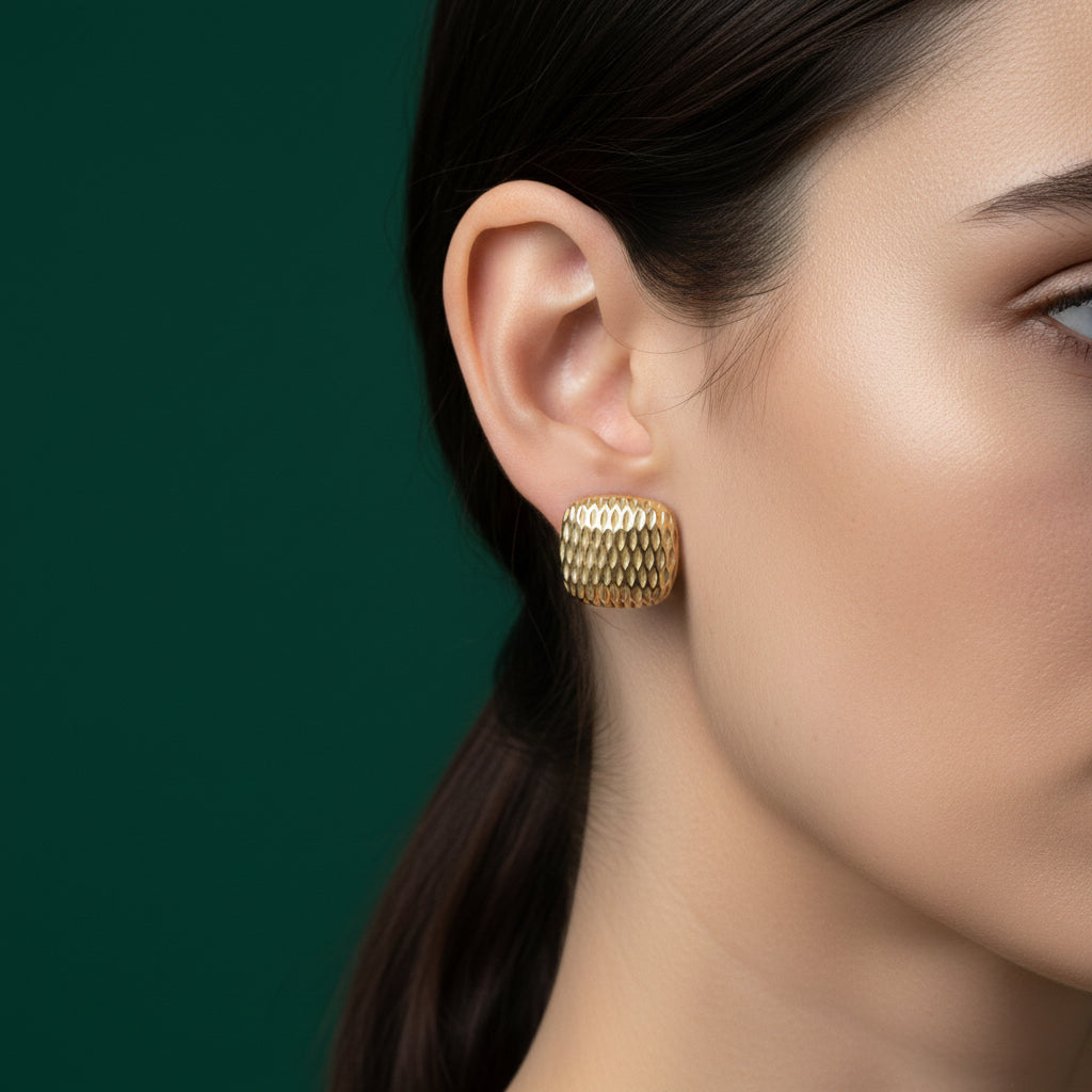 A woman with a low ponytail wearing medium-sized, 18K gold-plated rounded square stud earrings with a vertical ribbed fluted texture.