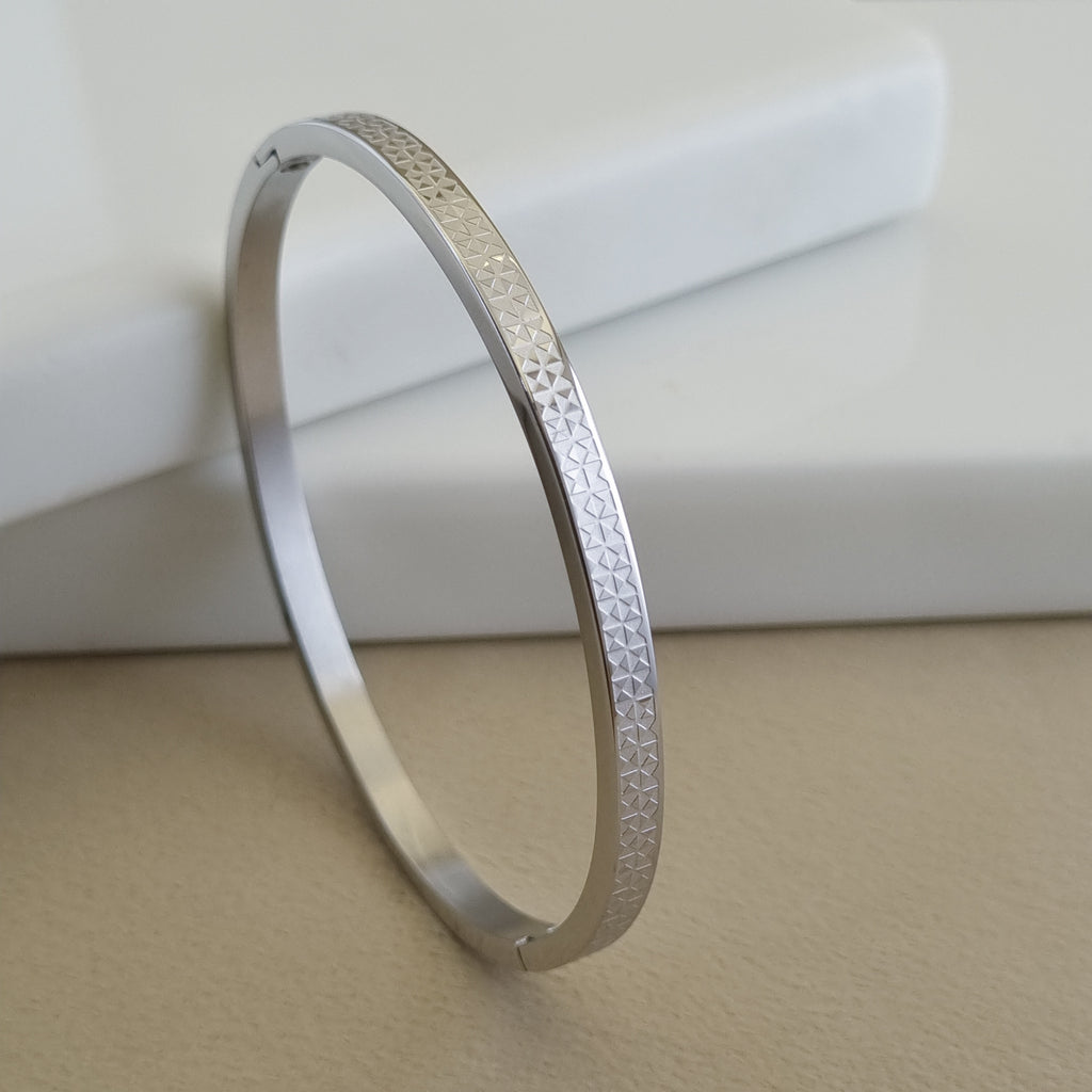 Treshire silver-tone Atlas bangle with micro-etched geometric texture displayed on a white marble surface.