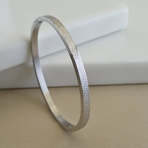 Treshire silver-tone Atlas bangle with micro-etched geometric texture displayed on a white marble surface.