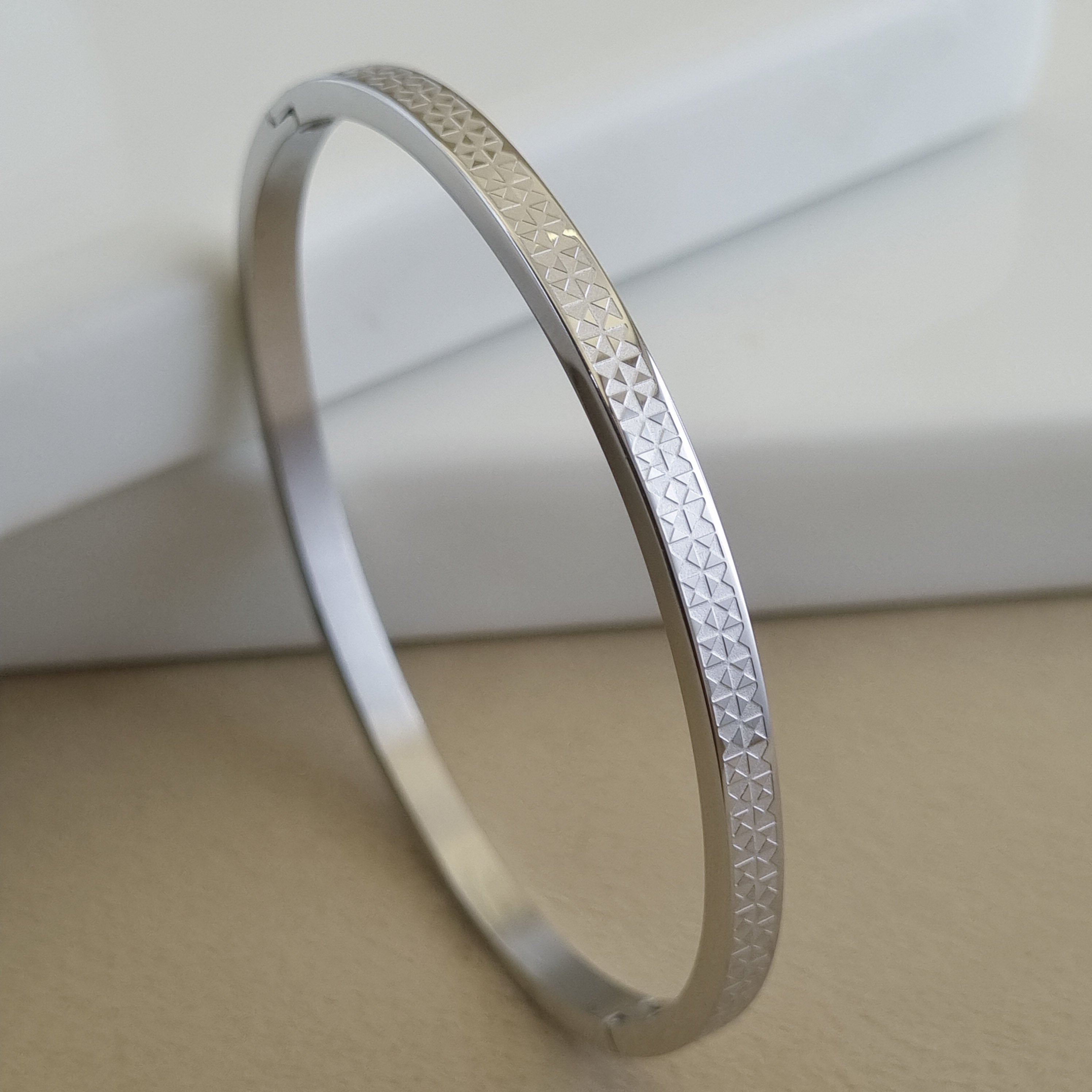 Treshire silver-tone Atlas bangle with micro-etched geometric texture displayed on a white marble surface.