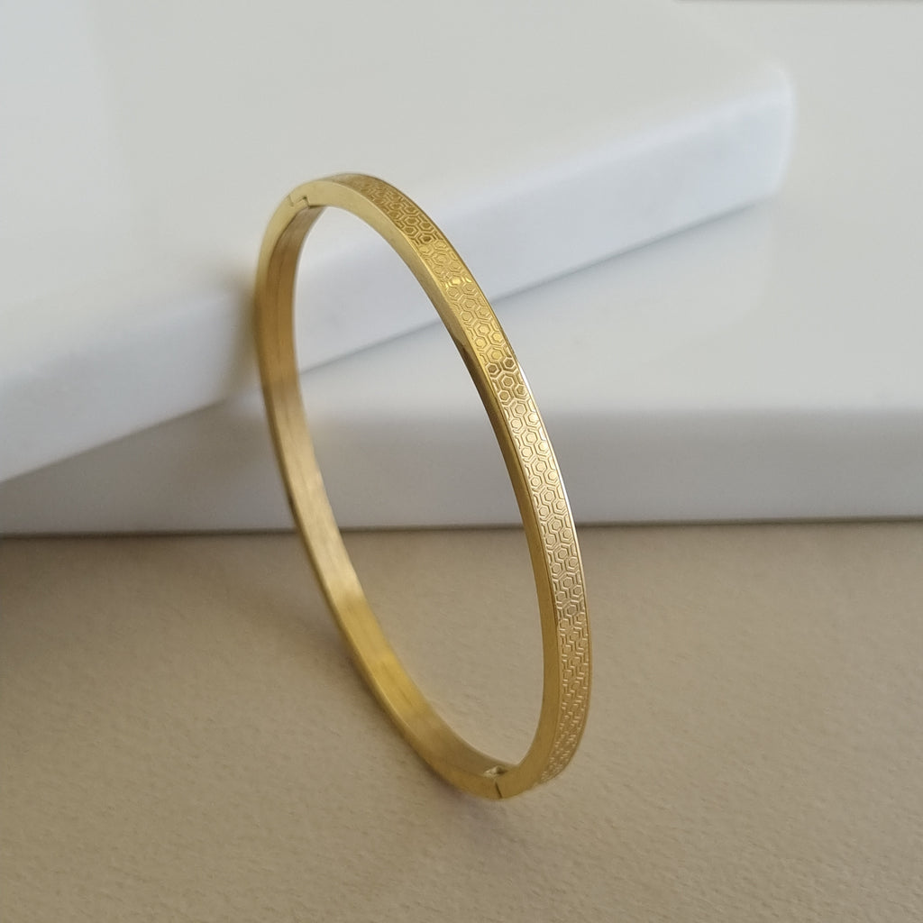 Treshire 18K gold plated Honeycomb bangle with a micro-etched hexagonal geometric pattern displayed on a white marble surface.