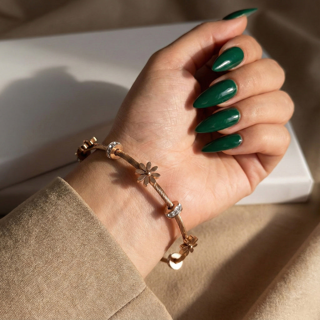 A woman's hand with green nails wearing an 18K rose gold-plated twisted cable bracelet with sculpted daisy charms and crystal spacers.