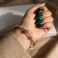A woman's hand with green nails wearing an 18K rose gold-plated twisted cable bracelet with sculpted daisy charms and crystal spacers.