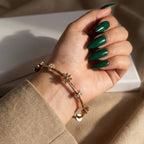 A woman's hand with green nails wearing an 18K rose gold-plated twisted cable bracelet with sculpted daisy charms and crystal spacers.