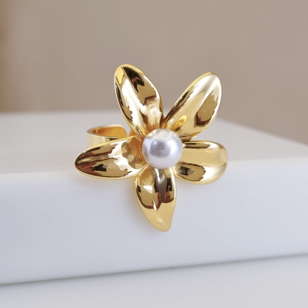 Gold flower-shaped ring with a pearl center on a white surface.