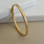 Treshire 18K gold plated Prism bangle with geometric faceted texture displayed on a white marble surface.