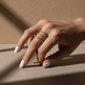A woman with white nails wearing an 18K gold-plated, size-adjustable hammered spiral wrap ring with crystal accents on her ring finger.