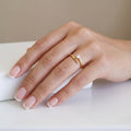 A high-polish 18K gold-plated, size-adjustable modern solitaire wrap ring with a single brilliant-cut crystal displayed on a woman's hand with a French manicure.