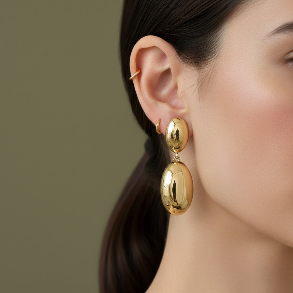A woman with a sleek low ponytail wearing large, 18K gold-plated double-tier oval sculptural drop earrings.