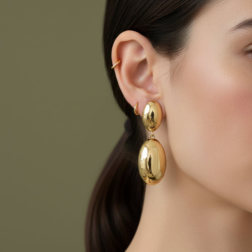 A woman with a sleek low ponytail wearing large, 18K gold-plated double-tier oval sculptural drop earrings.