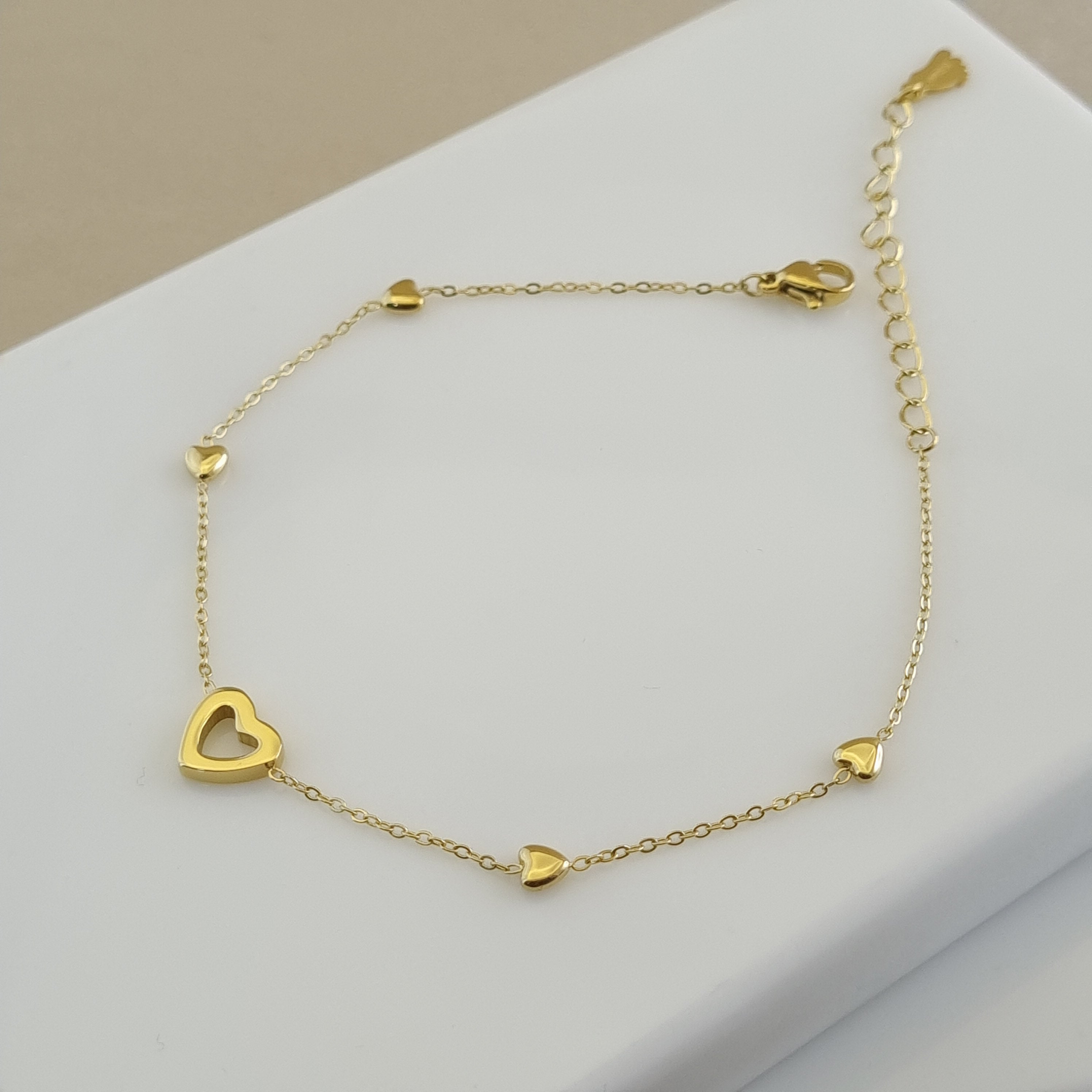 18K gold plated anklet with one open heart charm and four small solid heart charms on a delicate gold chain.