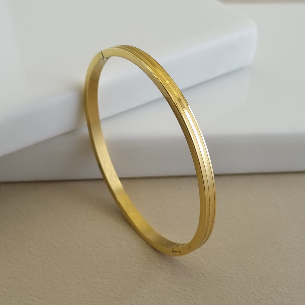 Treshire 18K gold plated Horizon Linear bangle with dual grooved detailing displayed on a white marble surface.