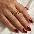 A woman with deep burgundy nails wearing an 18K gold-plated, size-adjustable triple spiral wrap ring on her middle finger.