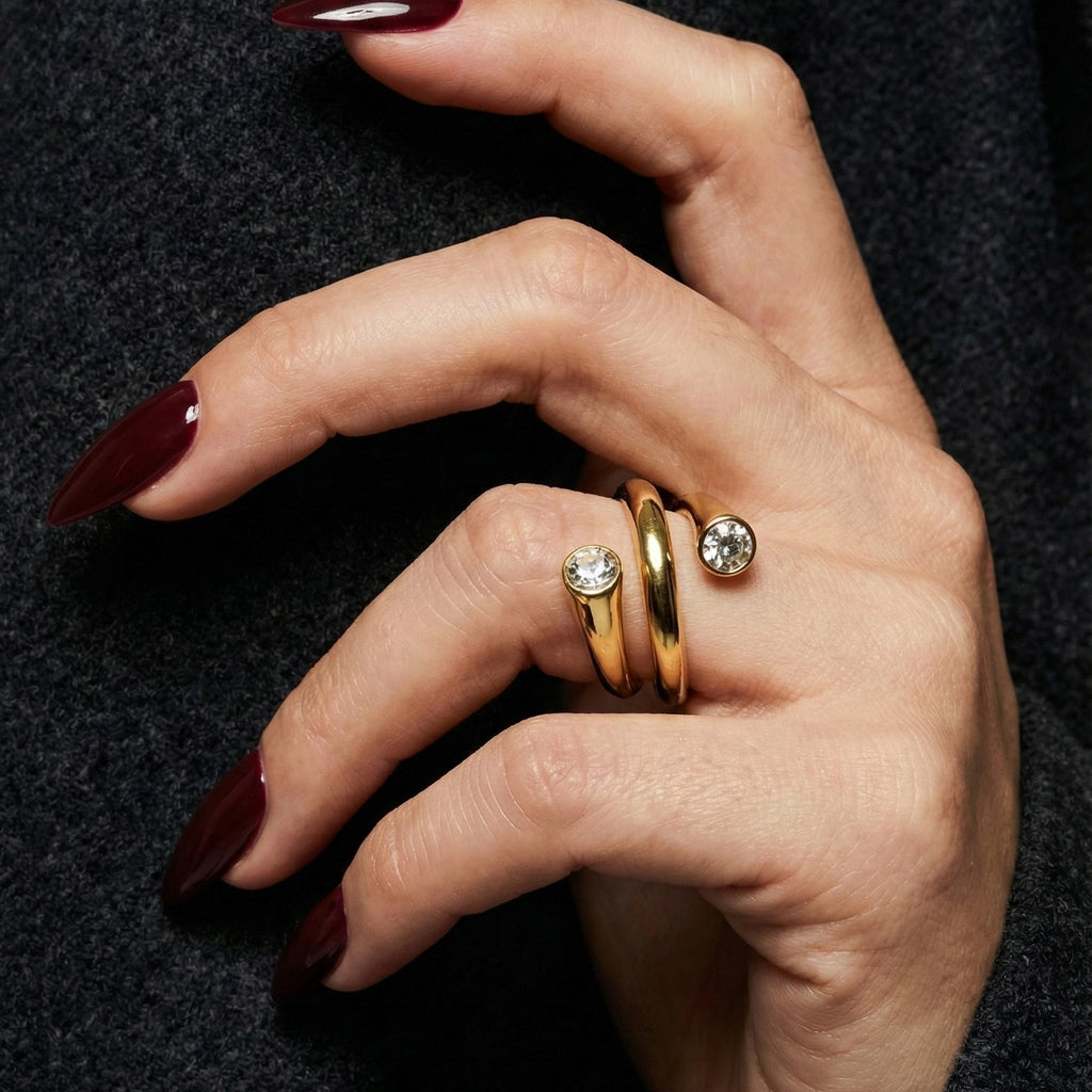 A woman with deep burgundy nails wearing an 18K gold-plated, size-adjustable spiral wrap ring featuring two brilliant-cut crystal terminals.