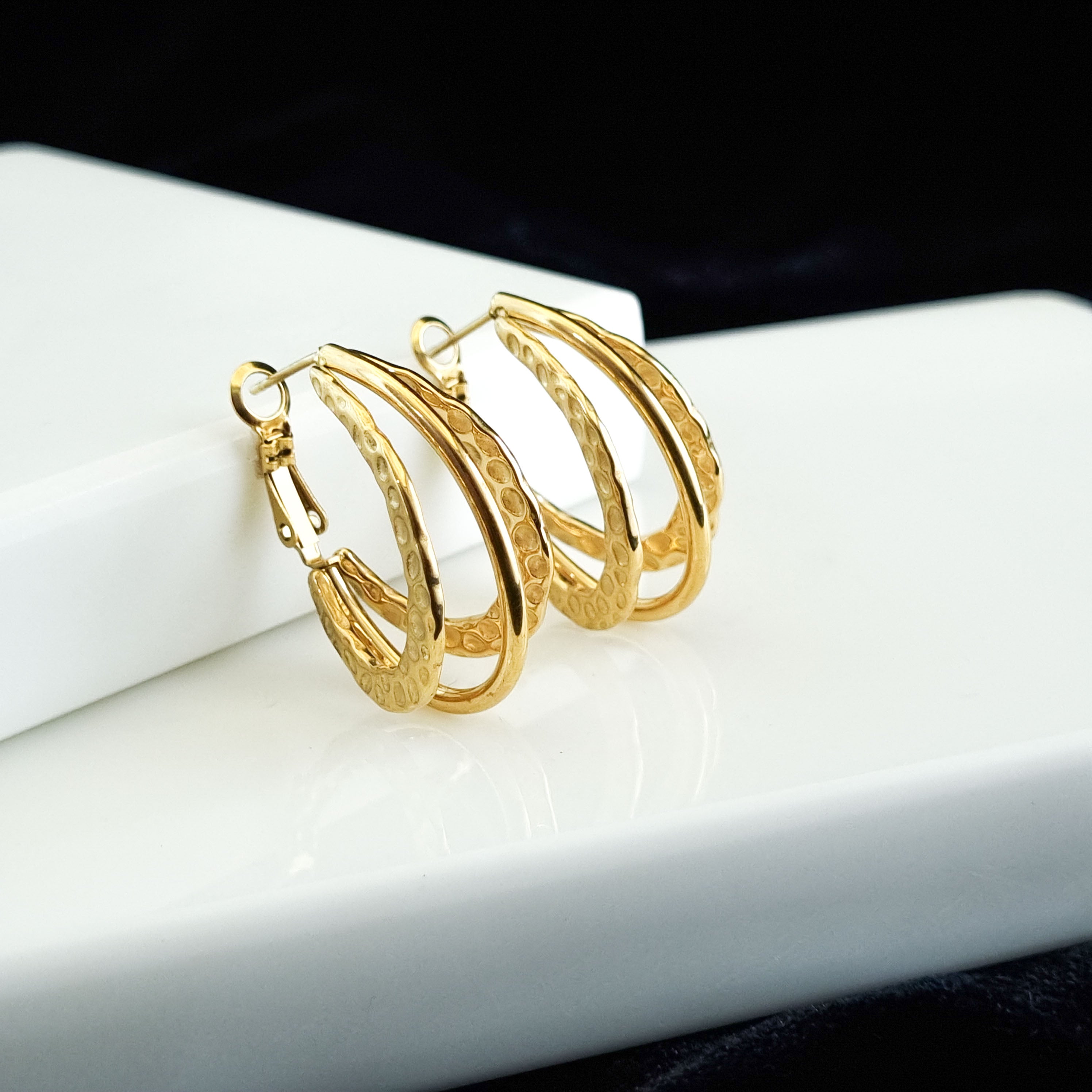 Gold hoop earrings on a white surface with a black background