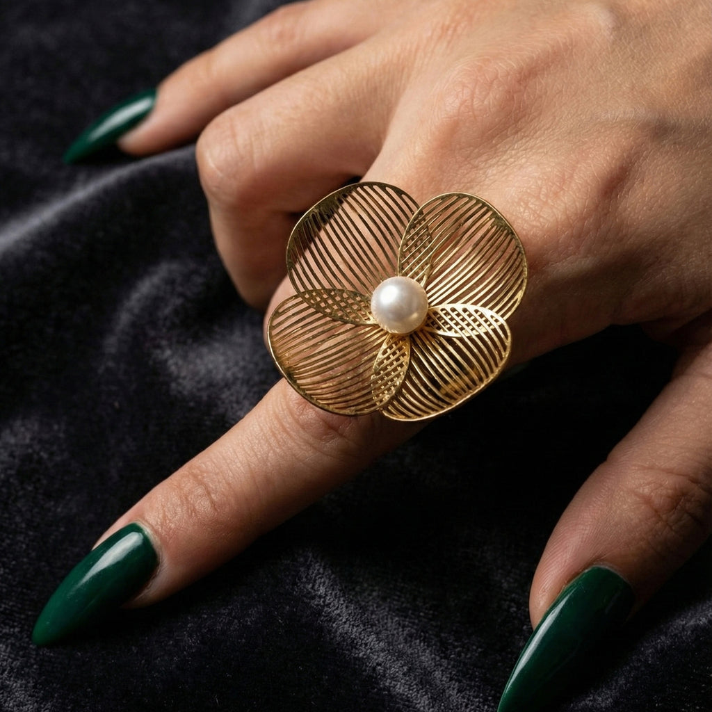 A woman with deep emerald green nails wearing a large 18K gold-plated, size-adjustable filigree flower statement ring with a central pearl on her index finger.