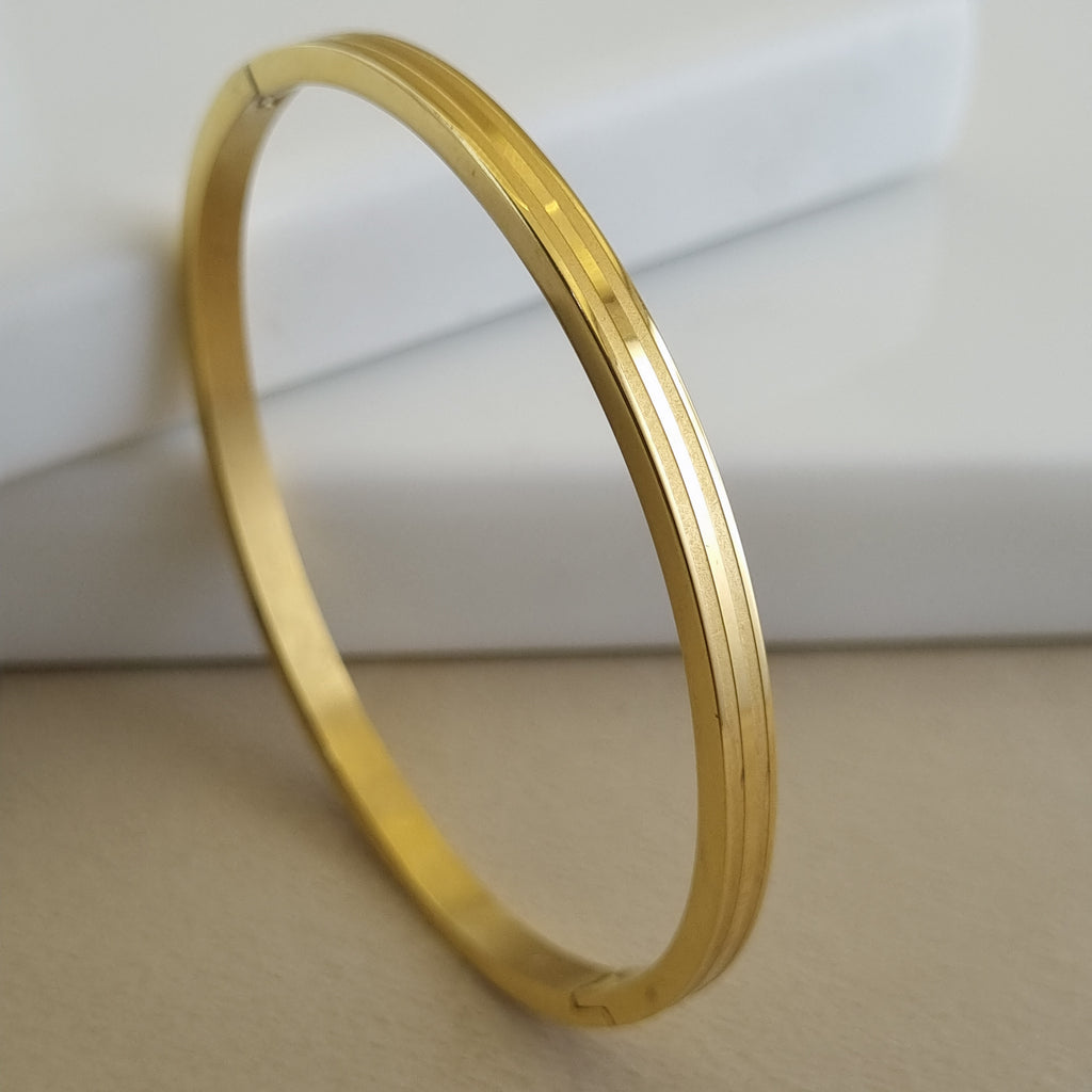 Treshire 18K gold plated Horizon Linear bangle with dual grooved detailing displayed on a white marble surface.
