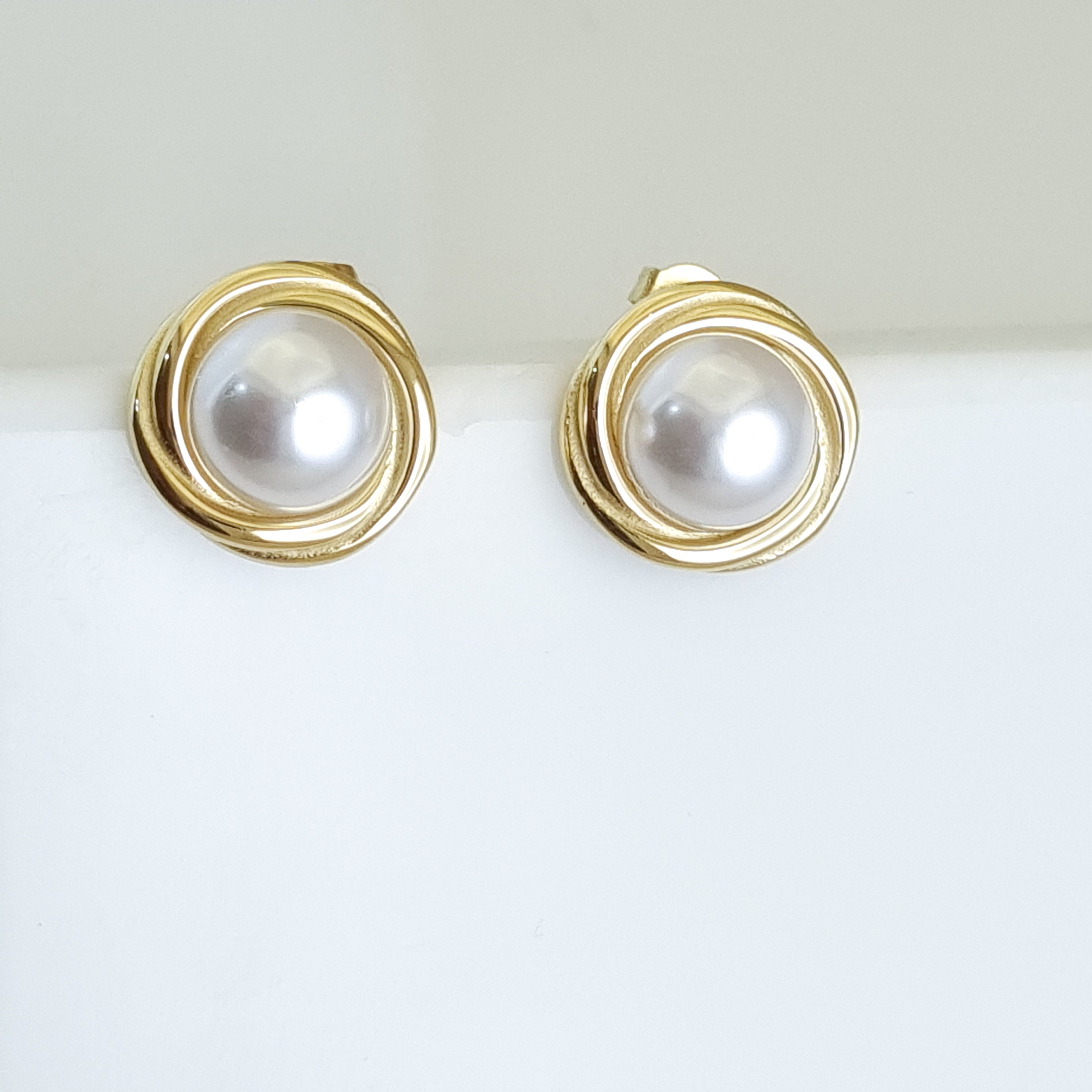 Gold earrings with pearl-like centers on a white background