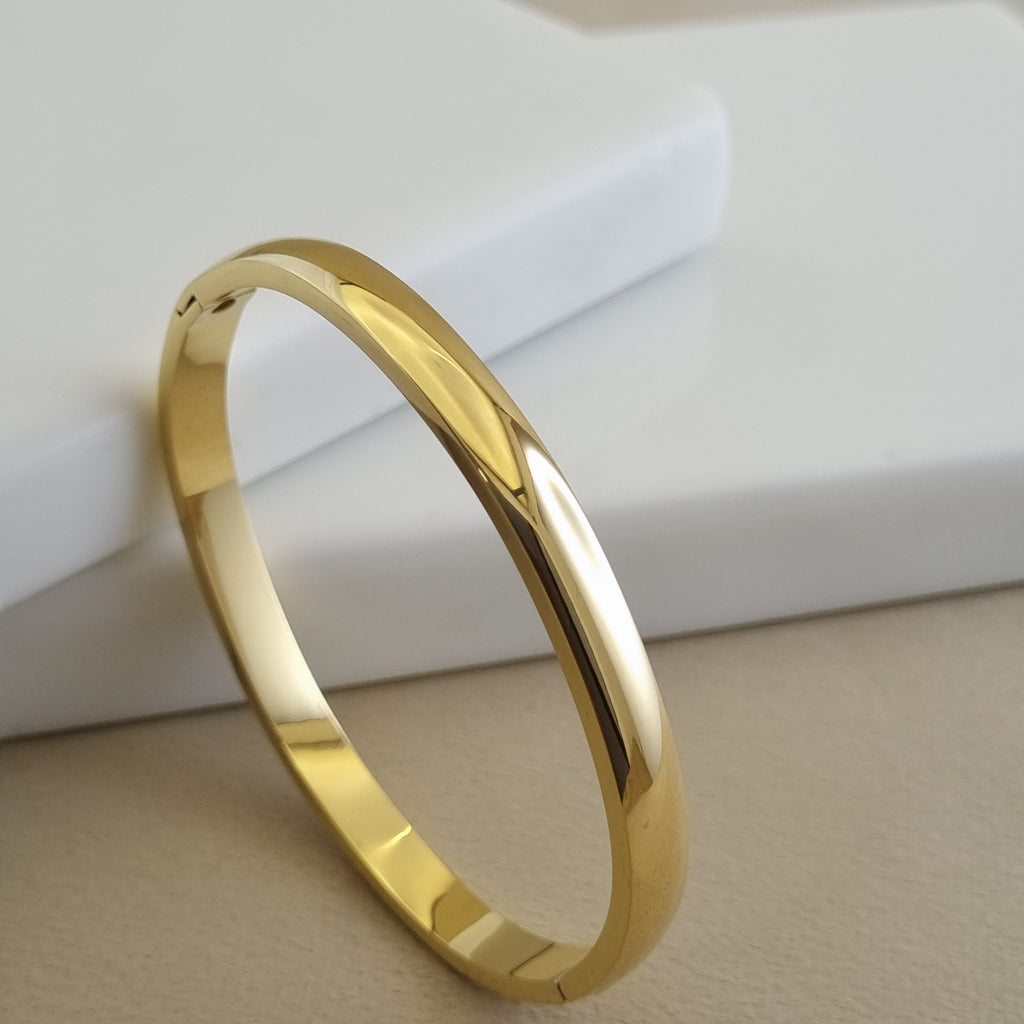 Treshire 18K gold plated Aurelia bangle with a smooth, high-polish mirror finish displayed on a white marble surface.