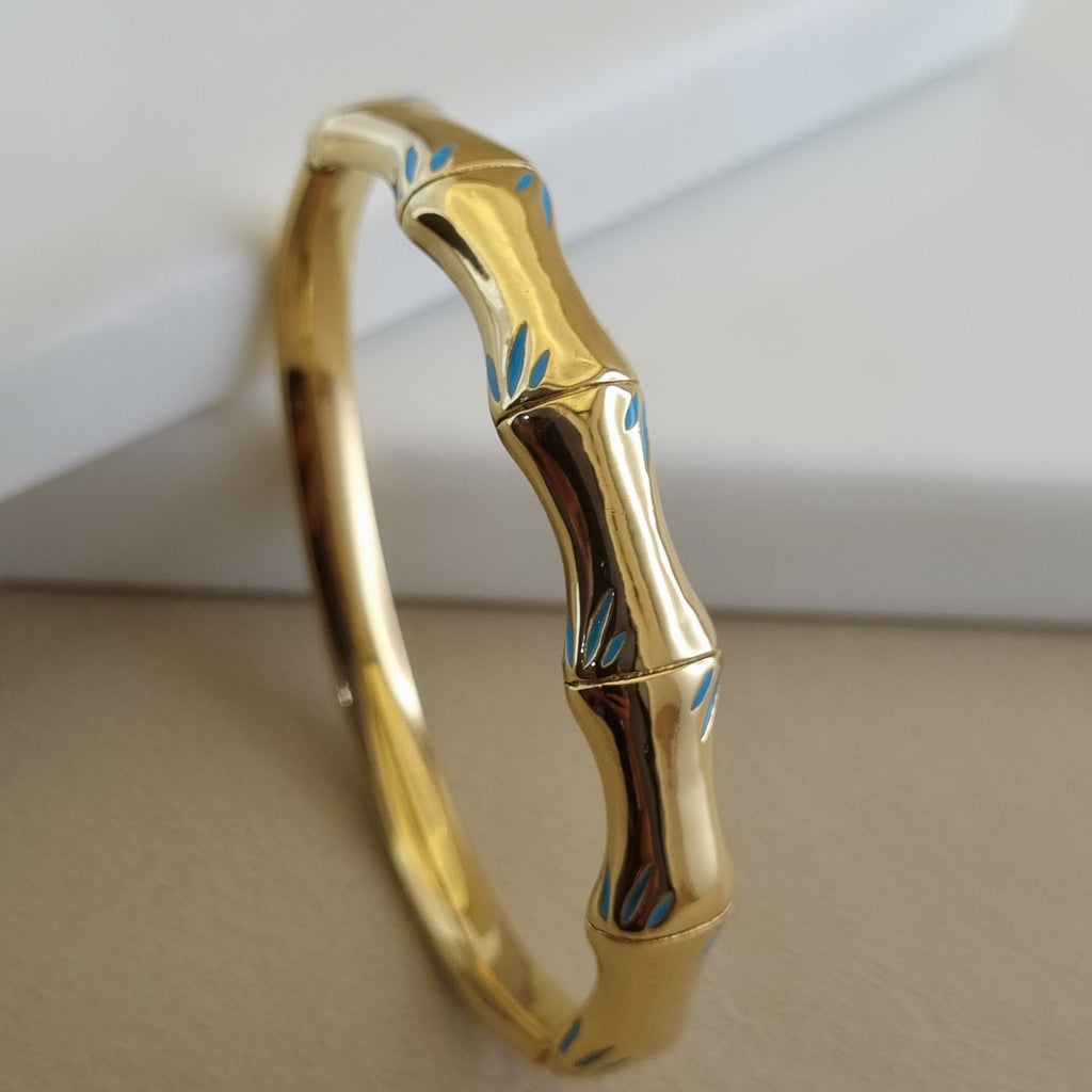 Treshire 18K gold plated Bamboo Breeze bangle featuring organic segmented nodes and blue enamel accents displayed on a white marble surface.